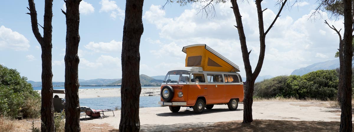 VW-T2-Bay-wtith-pop-top-roof-on-a-beach- VW T2 Bay parked by the beach with its pop-top roof elevated