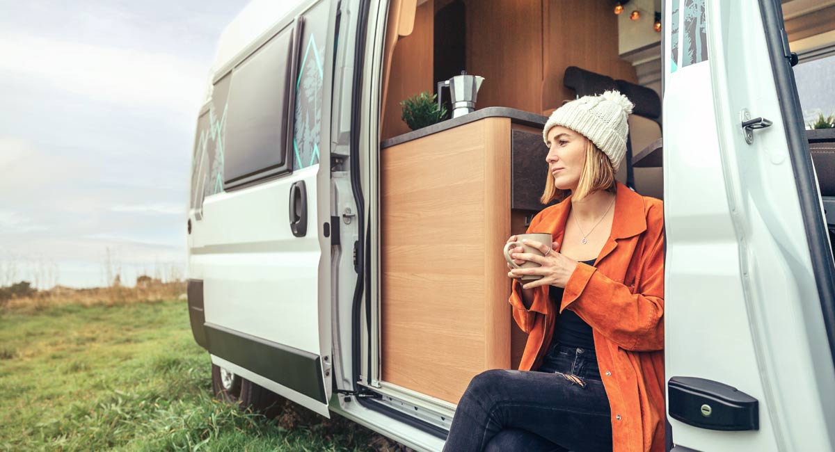 Woman sitting in a converted campervan holding a mug and looking outside