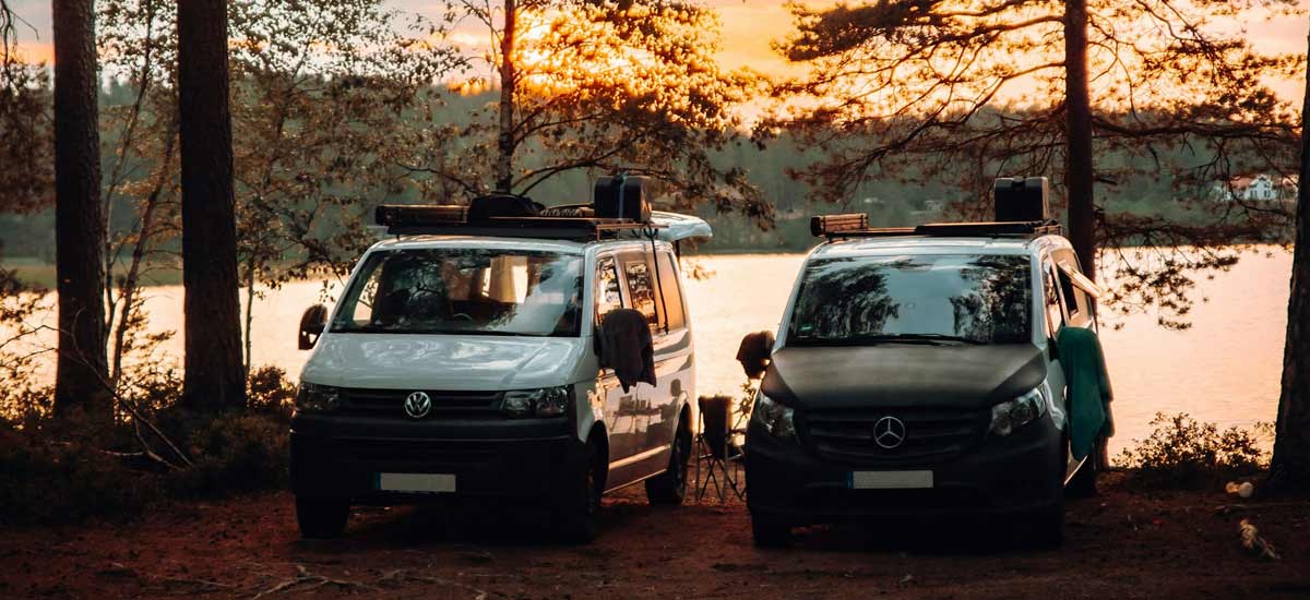 Two converted campervans by a lake at sunset