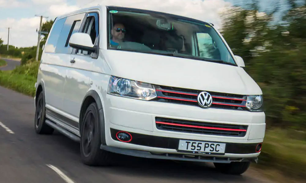 JKI25-Modern-Campervan-Insurance-Header-1 A white VW T5 Transporter in motion, driving down the road near Just Kampers