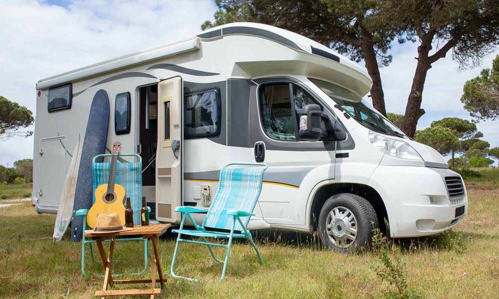 JKI25-Motorhome-Insurance-Header-1 A motorhome parked up at a camp site, with tables, chairs, and a guitar set up