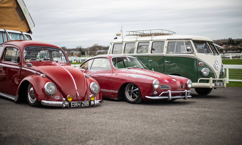 JKI25-CClassic-Air-Cooled-VW-Insurance-Header-1 A red VW Beetle, a red VW Karmann Ghia, and a green VW T2 Split Screen parked up at the Volkswagen show