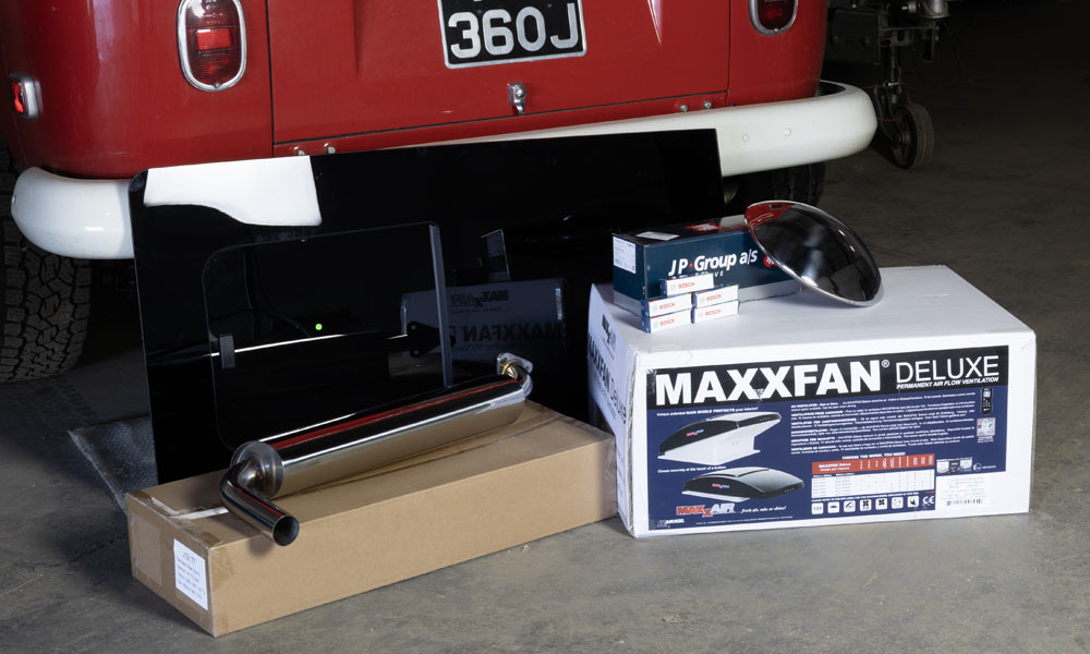 JKI25-Spare-Parts-Cover-Image-Header-1 A collection of spare parts placed behind a VW T2 camper, including an exhaust, a Maxxfan heater, and a tinted window