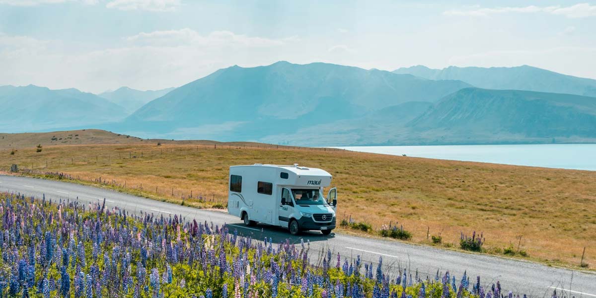 cost-to-run-a-motorhome-1 Motorhome driving by flowers and mountains - Cost to run a motorhome in the UK