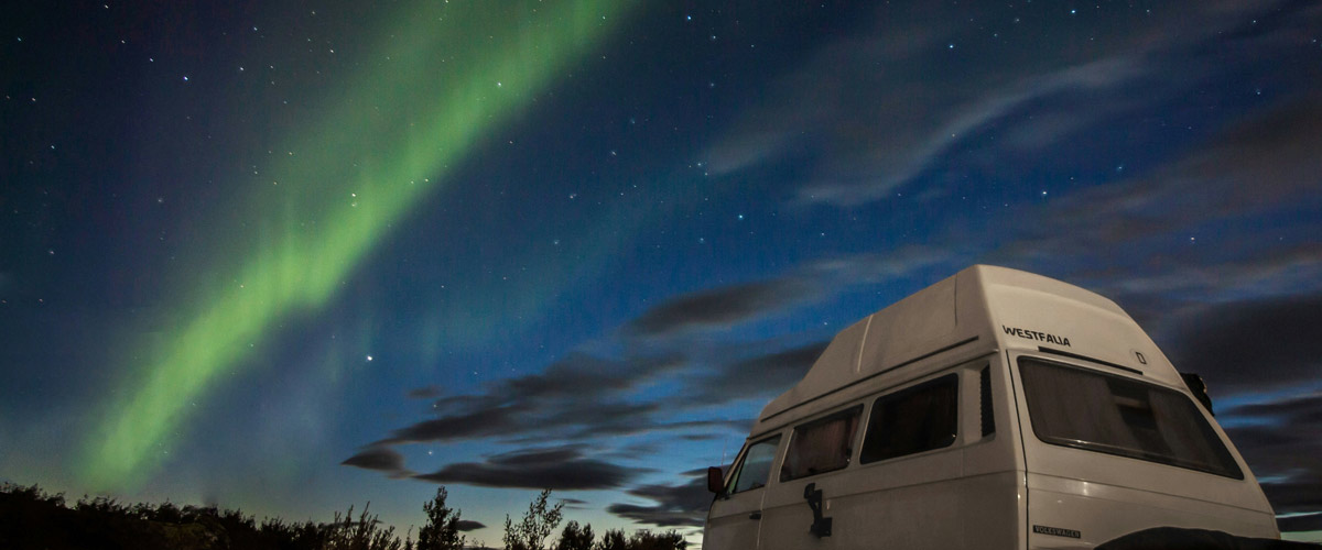 A white VW campervan under the Northern Lights