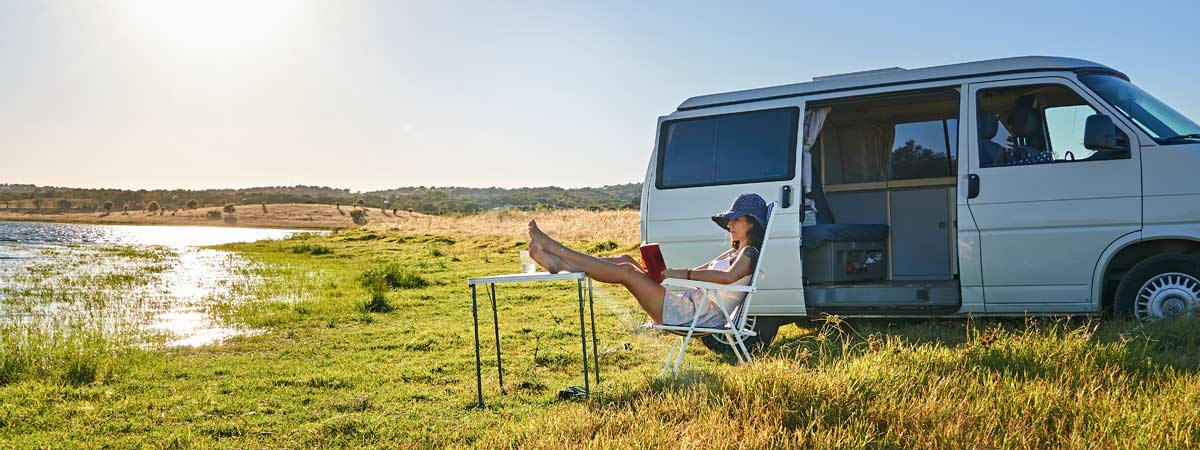 Lady sitting on a chair reading in front of a white campervan