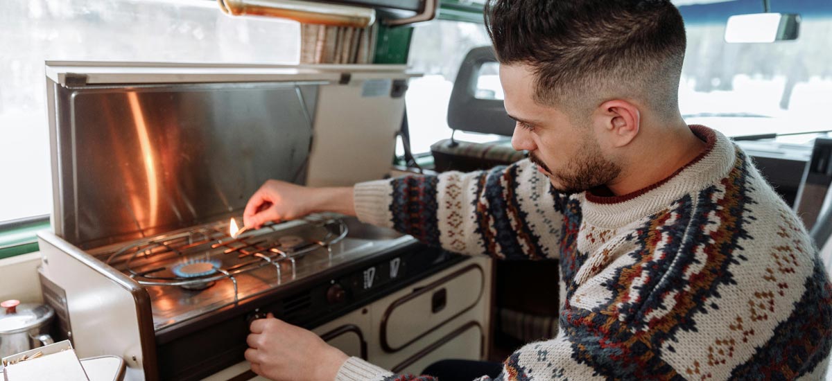 A man lighting a gas cooker inside a campervan