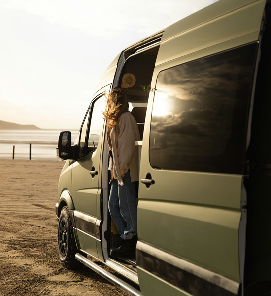 Lady loooking out of her campervan on the beach