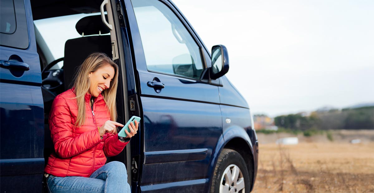 Smiling woman sitting in her campervan using her mobile phone