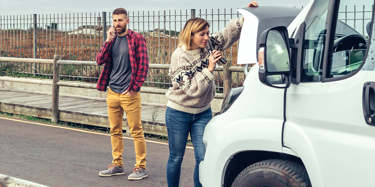 A couple with a broken down campervan, trying to fix the problem while calling for roadside assistance
