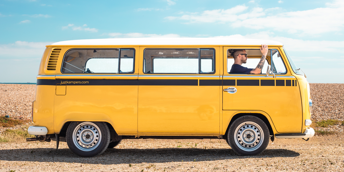 A yellow VW T2 Bay campervan parked up by the beach, with Josh from the Just Kampers team sitting in it