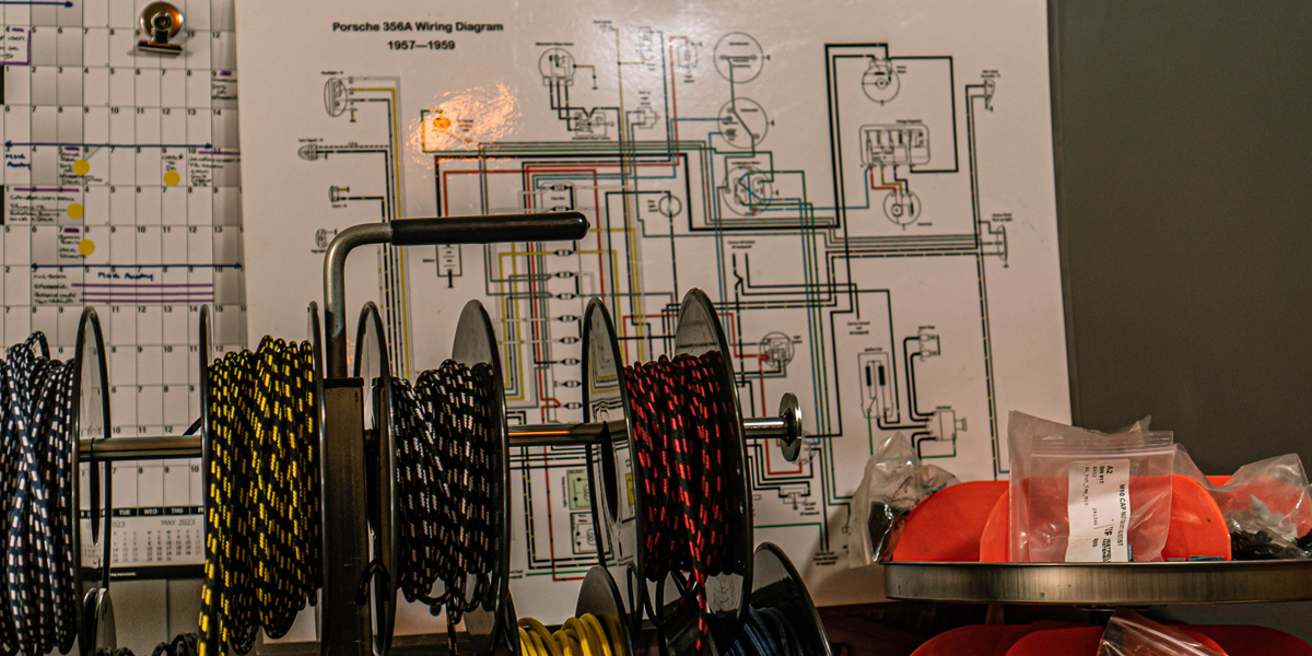 A selection of different automotive wires and cables on a workbench in front of a large wiring diagram on a workshop wall