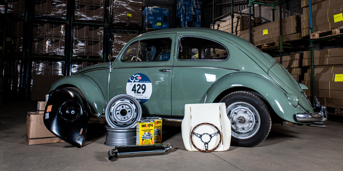 A green VW Beetle with a selection of spare parts and accessories piled up next to it