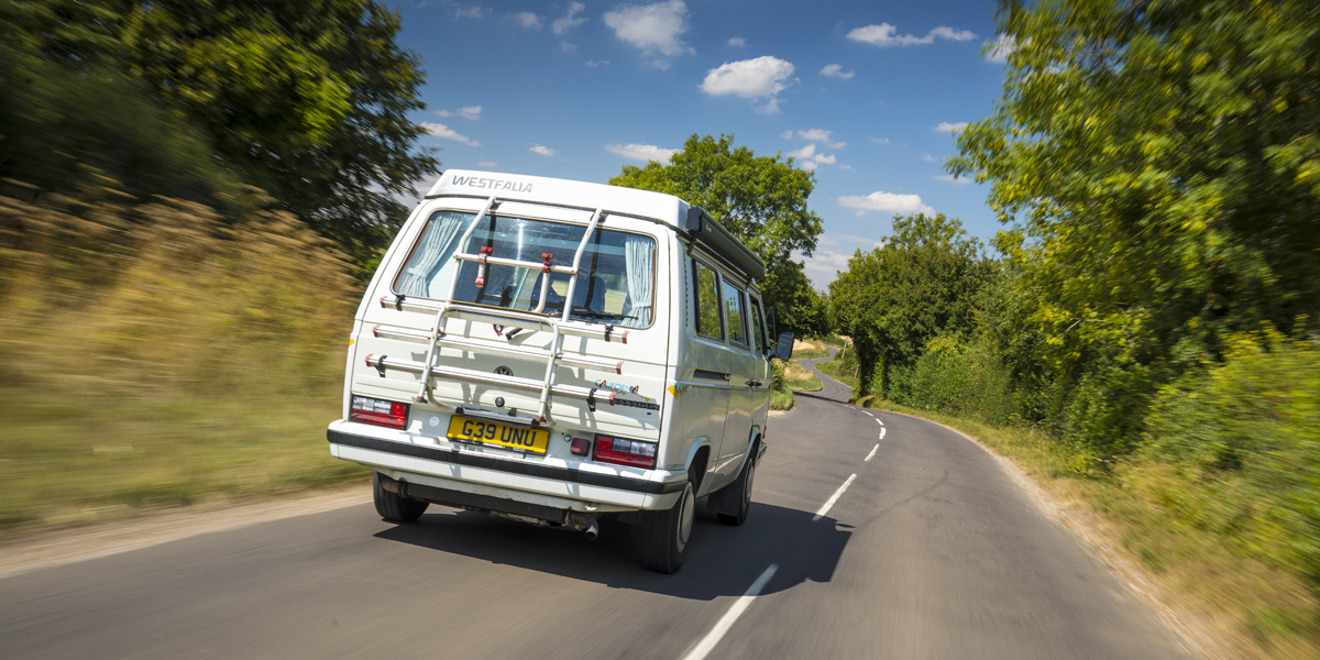 A VW T25 with a bike rack on the back, driving down a country lane