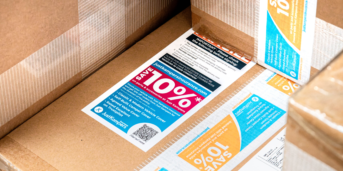 Several cardboard boxes ready to be dispatched from Just Kampers, with stickers and tape on, reminding people about the 10% discount they get for being insured with Just Kampers Insurance