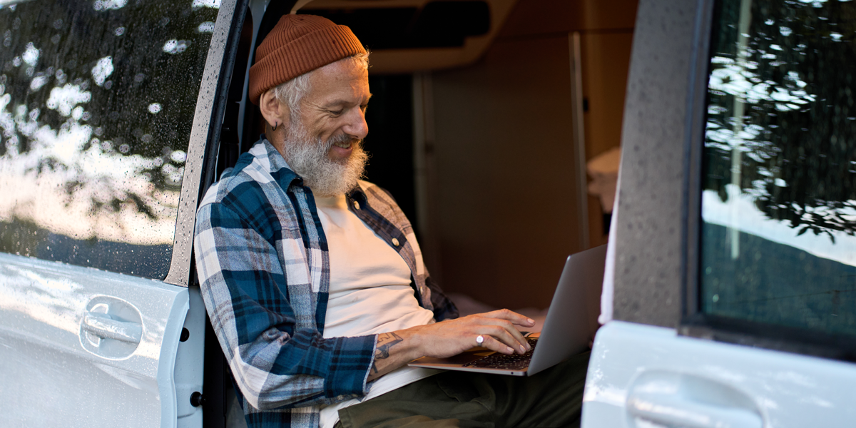 An older man, sat in his campervan while using his laptop
