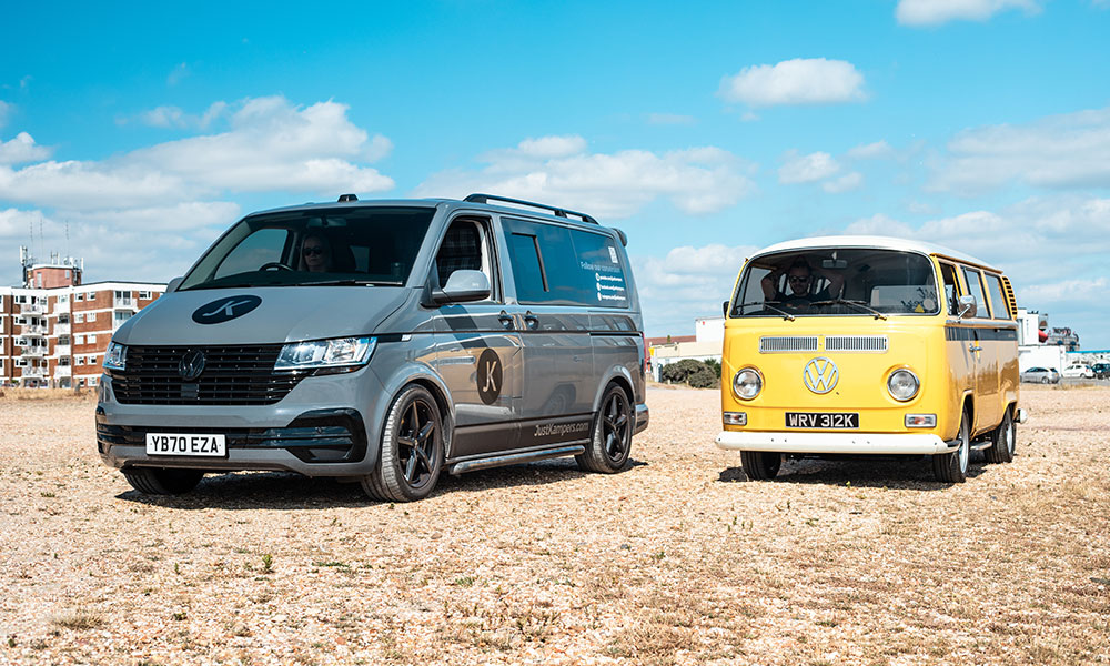 A modern VW T6 Transporter and a classic VW T2 Bay camper parked up on the beach together