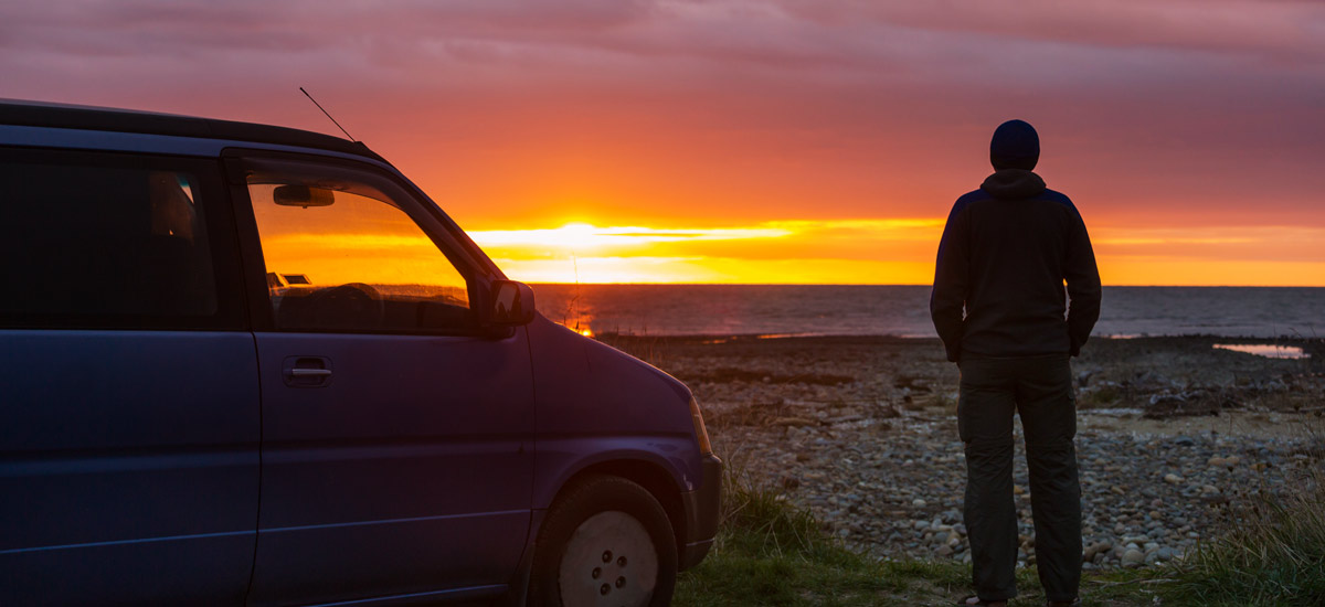 Person standing beside campervan watching the sunset over the sea